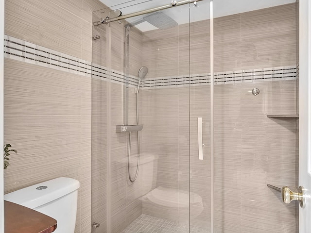 bathroom featuring toilet, a shower with shower door, and tile walls