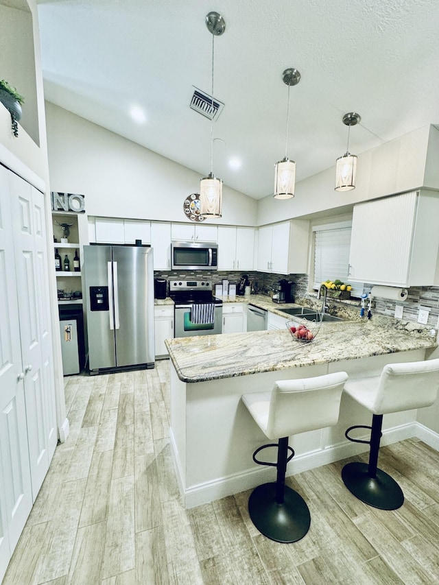 kitchen featuring lofted ceiling, white cabinets, sink, appliances with stainless steel finishes, and kitchen peninsula