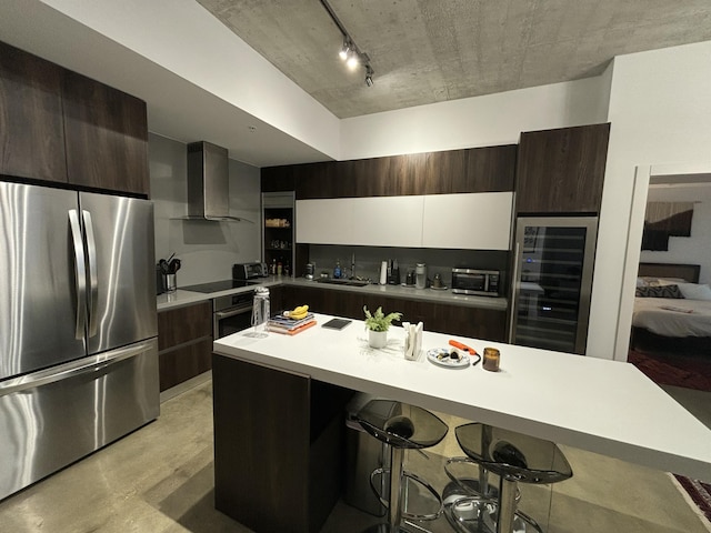 kitchen featuring wall chimney range hood, wine cooler, appliances with stainless steel finishes, white cabinetry, and a breakfast bar area