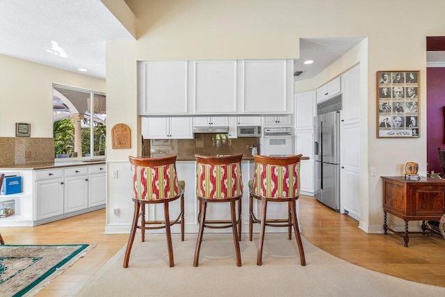 kitchen with white cabinetry, appliances with stainless steel finishes, backsplash, and a kitchen bar