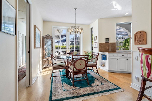 dining area featuring an inviting chandelier, french doors, a textured ceiling, and light wood-type flooring