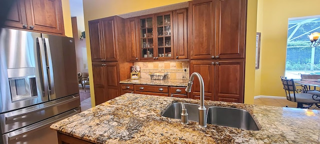 kitchen featuring sink, tasteful backsplash, light stone counters, tile patterned flooring, and stainless steel refrigerator with ice dispenser