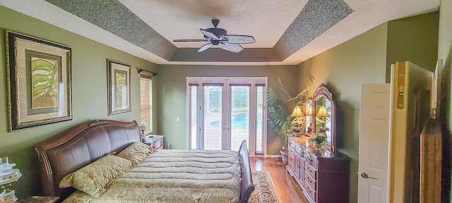 bedroom featuring ceiling fan, french doors, a raised ceiling, light hardwood / wood-style flooring, and a textured ceiling