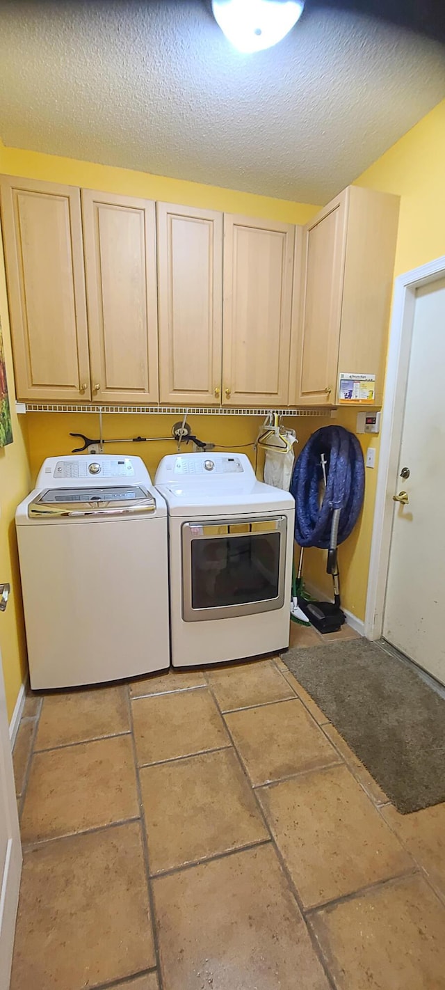 washroom featuring washing machine and dryer, light tile patterned floors, cabinets, and a textured ceiling