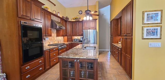 kitchen featuring sink, light stone counters, range hood, a center island with sink, and appliances with stainless steel finishes