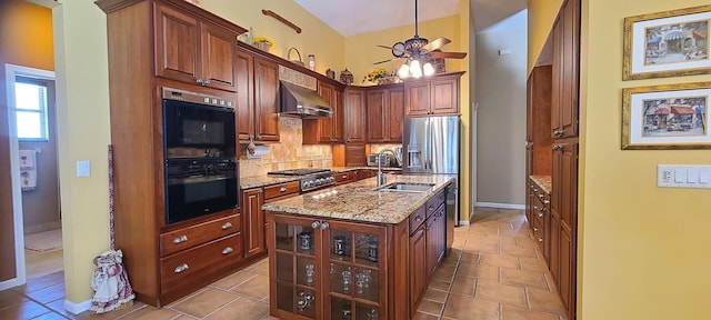 kitchen featuring light stone countertops, sink, black double oven, a center island with sink, and exhaust hood