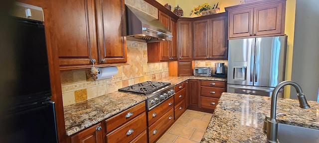 kitchen with decorative backsplash, light stone countertops, stainless steel appliances, and wall chimney range hood