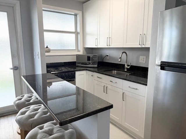 kitchen with dark stone counters, sink, white cabinets, and stainless steel appliances