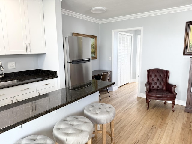 kitchen with white cabinetry, sink, stainless steel fridge, light hardwood / wood-style floors, and ornamental molding