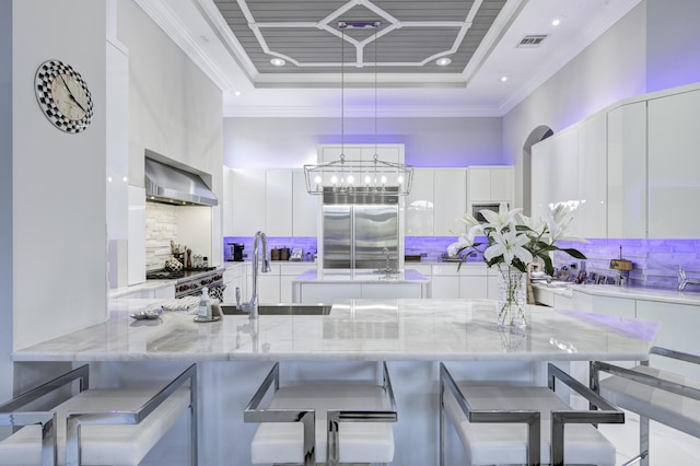 kitchen with a kitchen breakfast bar, stainless steel built in fridge, wall chimney range hood, decorative light fixtures, and white cabinetry