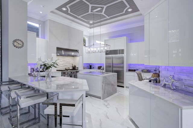 kitchen featuring high end appliances, white cabinets, hanging light fixtures, wall chimney exhaust hood, and kitchen peninsula