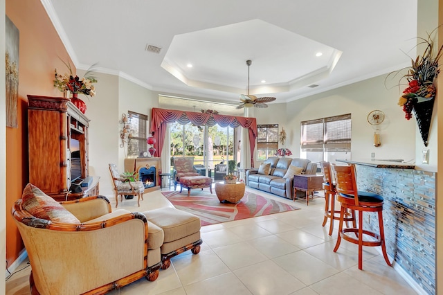 living room featuring light tile patterned floors, a tray ceiling, ceiling fan, and ornamental molding