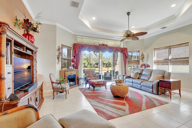 living room featuring a tray ceiling, ceiling fan, light tile patterned floors, and ornamental molding