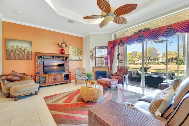 living room featuring a tray ceiling, tile patterned floors, ceiling fan, and crown molding