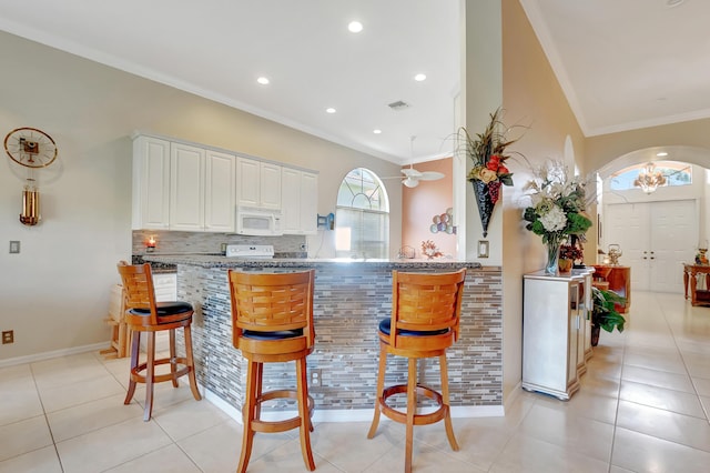 kitchen featuring kitchen peninsula, a kitchen bar, white appliances, and light tile patterned floors