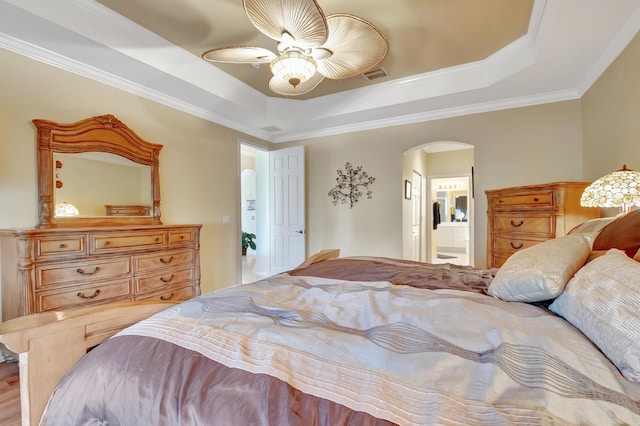 bedroom featuring ceiling fan, a raised ceiling, crown molding, and ensuite bath