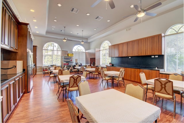 dining room with light hardwood / wood-style floors, a raised ceiling, and ceiling fan