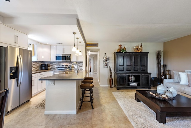 kitchen with pendant lighting, white cabinets, a kitchen breakfast bar, decorative backsplash, and appliances with stainless steel finishes