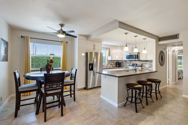 kitchen featuring kitchen peninsula, decorative backsplash, stainless steel appliances, pendant lighting, and white cabinets