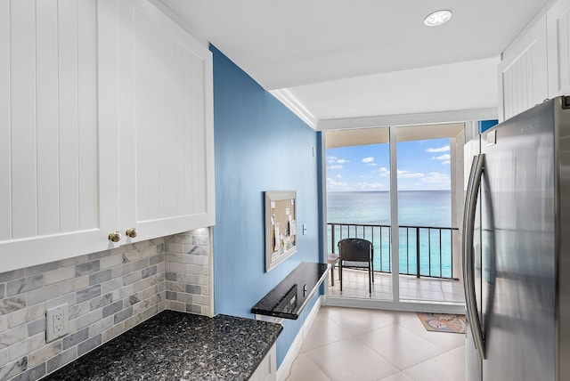 kitchen featuring stainless steel fridge, tasteful backsplash, dark stone counters, a water view, and white cabinets