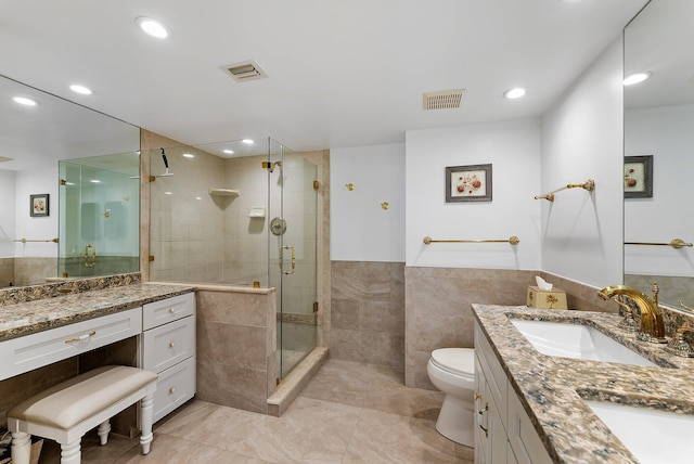 bathroom with vanity, toilet, a shower with door, and tile walls