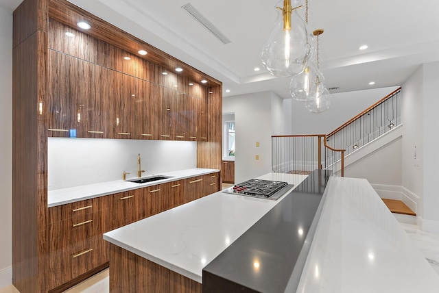 kitchen with decorative light fixtures, a kitchen island, sink, and stainless steel gas cooktop