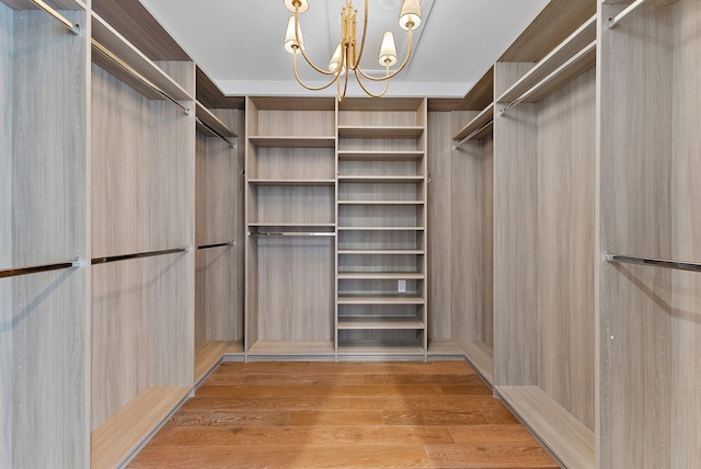 spacious closet with light hardwood / wood-style floors and a notable chandelier