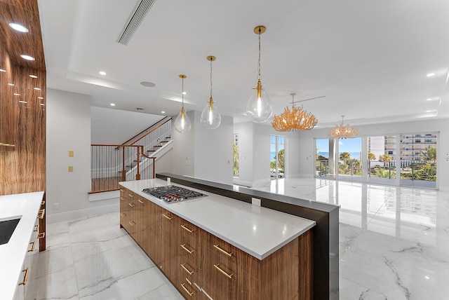 kitchen with stainless steel gas cooktop, a notable chandelier, pendant lighting, a spacious island, and a tray ceiling