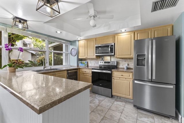 kitchen featuring a raised ceiling, kitchen peninsula, ceiling fan, and appliances with stainless steel finishes