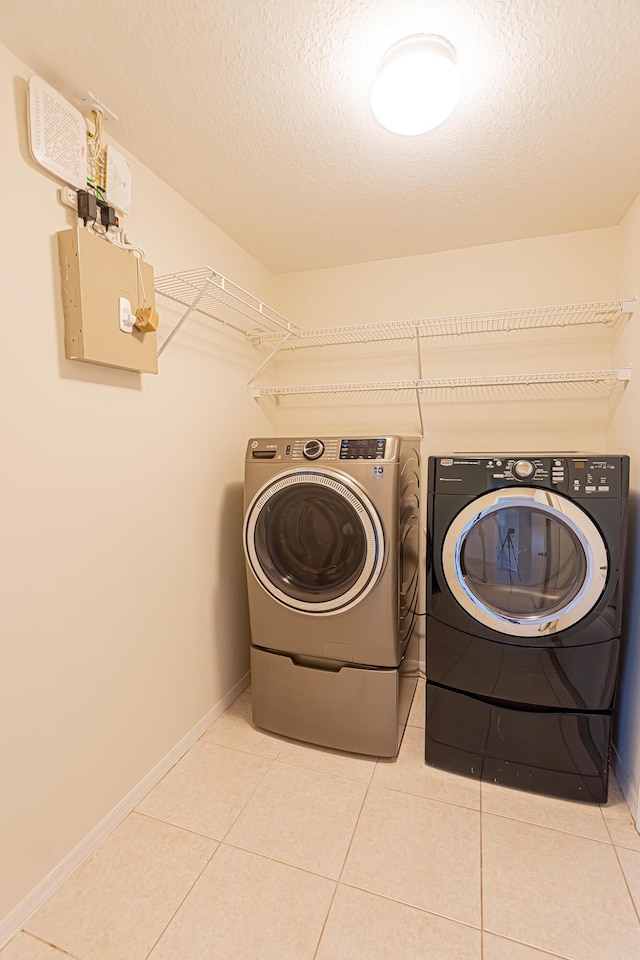 washroom with washing machine and dryer, light tile patterned flooring, and a textured ceiling