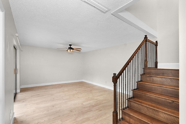 staircase with ceiling fan, wood-type flooring, and a textured ceiling