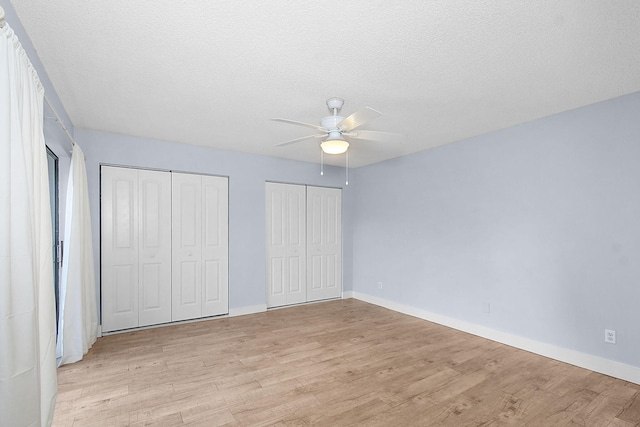 unfurnished bedroom featuring ceiling fan, light hardwood / wood-style floors, a textured ceiling, and two closets