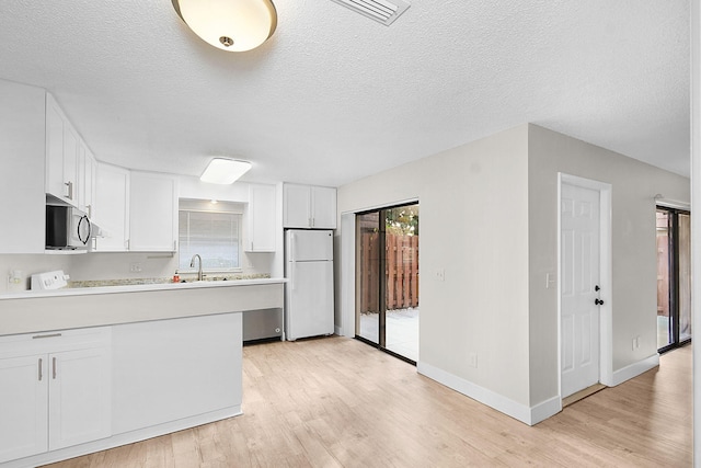 kitchen featuring white refrigerator, light hardwood / wood-style flooring, white cabinetry, and a healthy amount of sunlight