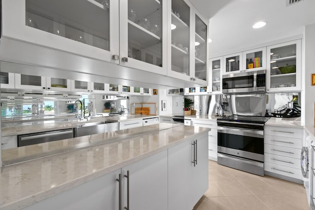 kitchen featuring sink, stainless steel appliances, white cabinets, light stone counters, and light tile patterned flooring