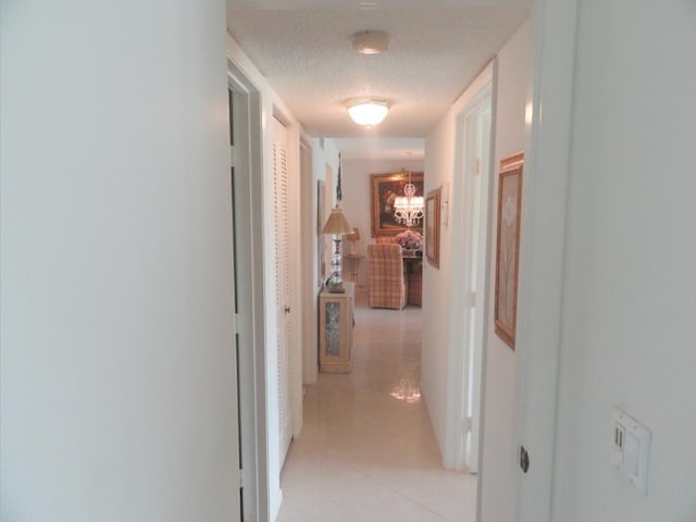 hall with light tile patterned floors, a textured ceiling, and a chandelier