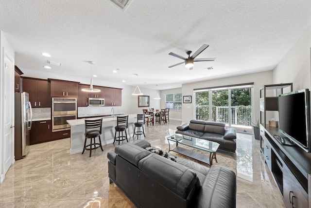 living room with ceiling fan, sink, and a textured ceiling