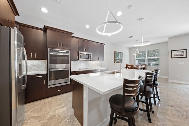 kitchen featuring dark brown cabinetry, sink, hanging light fixtures, stainless steel appliances, and a kitchen island with sink