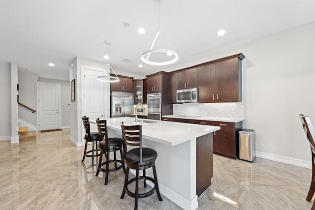 kitchen featuring sink, an island with sink, decorative light fixtures, dark brown cabinets, and stainless steel appliances