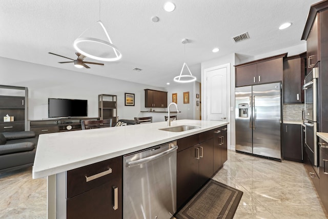 kitchen with a textured ceiling, stainless steel appliances, sink, pendant lighting, and an island with sink