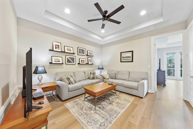 living room featuring a tray ceiling, ceiling fan, and light hardwood / wood-style floors