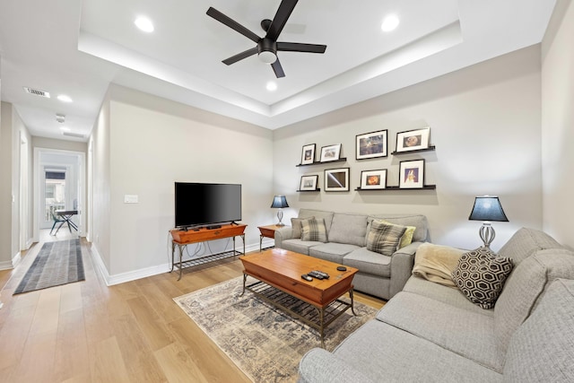 living room featuring a tray ceiling, ceiling fan, and light wood-type flooring