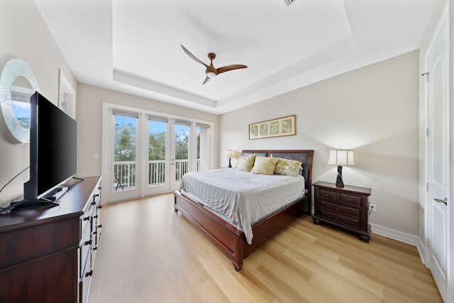 bedroom with access to outside, light hardwood / wood-style flooring, ceiling fan, and a tray ceiling