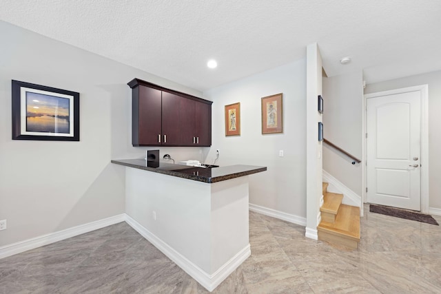 kitchen with kitchen peninsula, dark brown cabinets, a textured ceiling, and dark stone countertops