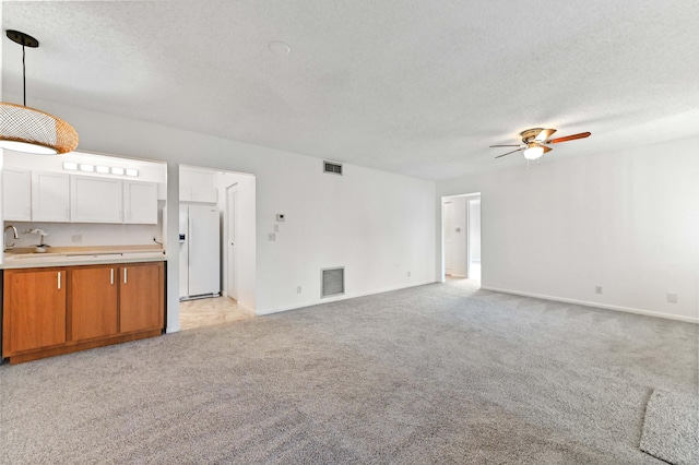 unfurnished living room with ceiling fan, light colored carpet, sink, and a textured ceiling