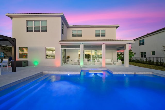 back house at dusk featuring a fenced in pool and a patio