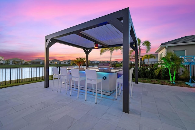 patio terrace at dusk with a bar, a water view, a grill, and a gazebo