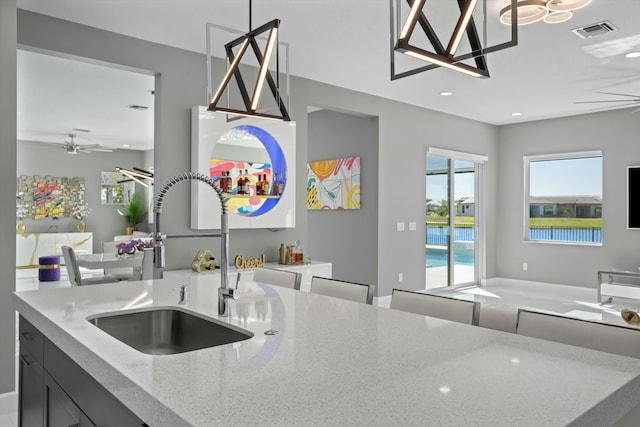 kitchen featuring light stone counters, sink, decorative light fixtures, and ceiling fan