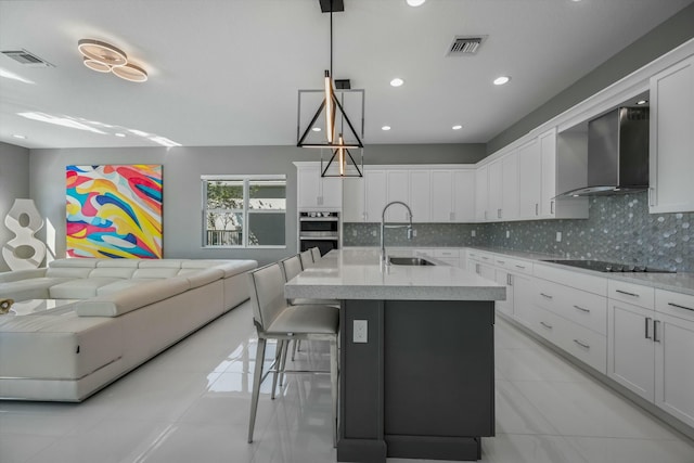 kitchen with sink, white cabinets, hanging light fixtures, black electric stovetop, and wall chimney exhaust hood