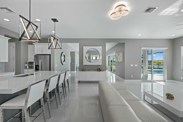 kitchen with a breakfast bar, decorative light fixtures, white cabinetry, sink, and stainless steel fridge with ice dispenser