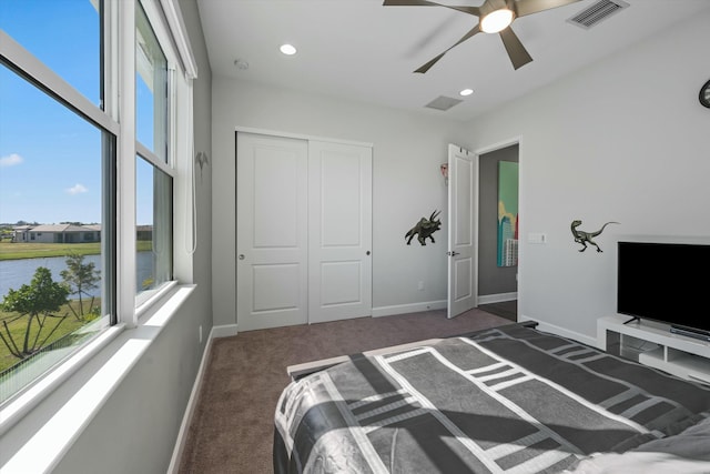 carpeted bedroom with multiple windows, a closet, ceiling fan, and a water view